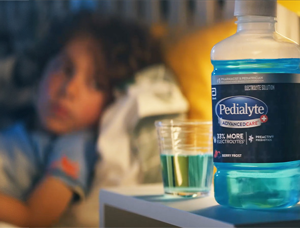 Child in bed looking at blue Pedialyte liter with electrolytes to help hydrate during stomach flu symptoms.